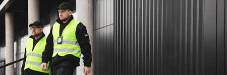 Policemen in reflective vests looking around carefully during patrol in the city centerの写真素材