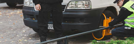 Two policeman setting a wheel clamp on a wrong parked carの写真素材