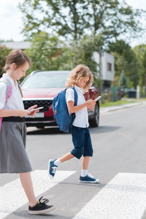 School boy and a girl cross the street looking at the phonesの写真素材