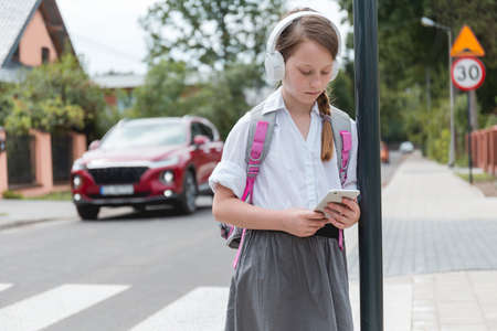 Schoolgirl with headphones and tablet is standing in the streetの写真素材
