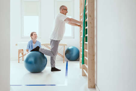 Young professional physiotherapist exercising with an injured patient using a blue ball