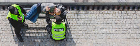 Police officers during patrol next to homeless man lying on the bench in the cityの写真素材