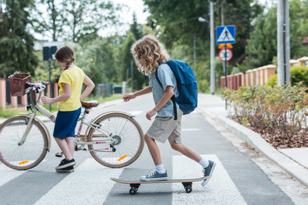 Boy on a skateboard and a girl with a bicycle cross the streetの写真素材