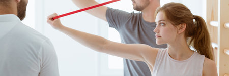 Young man and a woman stretch their arms with the use of tapes during classes with a physiotherapistの写真素材