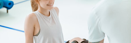 Teenage girl after car accident with orthosis on the leg exercises on blue mat in the company of physiotherapistの写真素材
