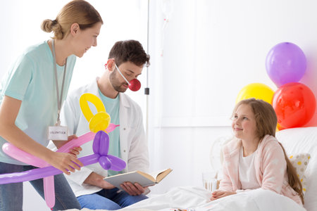 Hospital clown and volunteer reading a book to sick little girlの写真素材