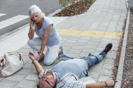 Mature couple talking on mobile phone in the street. They are lying on the sidewalk.の写真素材