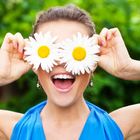 attractive young adult covering her eyes with white chamomile and laugh out loudlyの写真素材