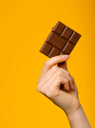 beautiful female hand holding milk chocolate bar isolated on yellow background