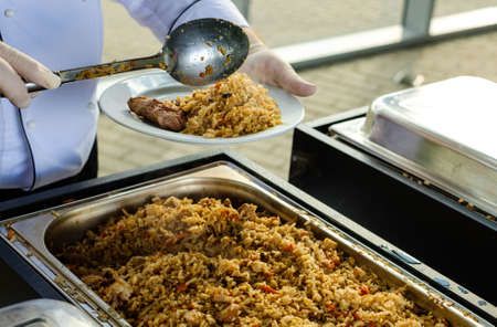 Waiter's hands in sterile gloves put food on white dish for a event with cateringの写真素材
