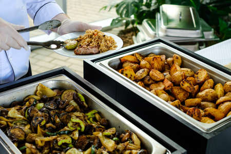 Waiter's hands in sterile gloves put food on white dish for a event with catering