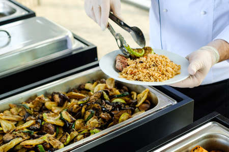 Waiter's hands in sterile gloves put food on white dish for a event with cateringの写真素材