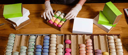 Female hands in gloves packs traditional french dessert macaroon in paper boxes for delieveryの写真素材