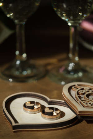 Golden wedding rings in a wooden box carved in a shape of heart with champagne glass on a background. Wedding celebration conceptの写真素材