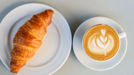 Top view on plates with croissant and latte with latte art on white tableの写真素材