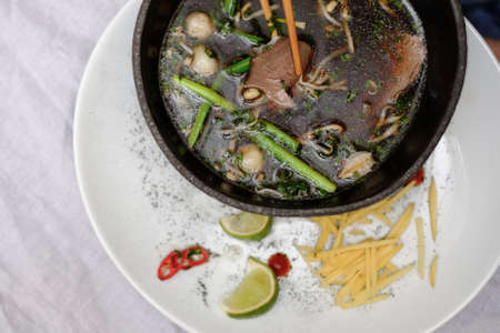 Traditional vietnamese pho bo soup with vegetables and beef in black bowl on white plate