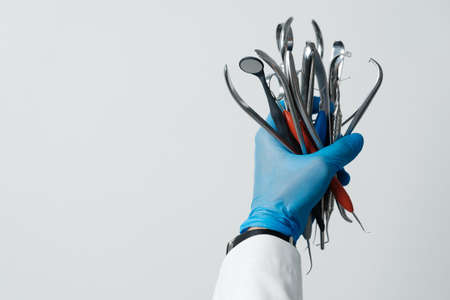 The dentists hand in a blue glove holds bunch of dental instruments, dental mirror, tweezers, probe...