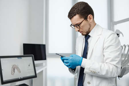 Handsome male dentist using smartphone in dental officeの写真素材