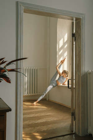 Fitness, yoga, stretching and healthy lifestyle concept - young woman doing exercises near window at homeの写真素材