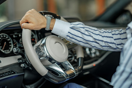Close up view of male hand holding steering wheel of a luxury car. Man wears an expensive watch and...