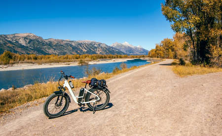 white e-bike parked next to winding blue snake river with teton mountains in the backgroundの写真素材