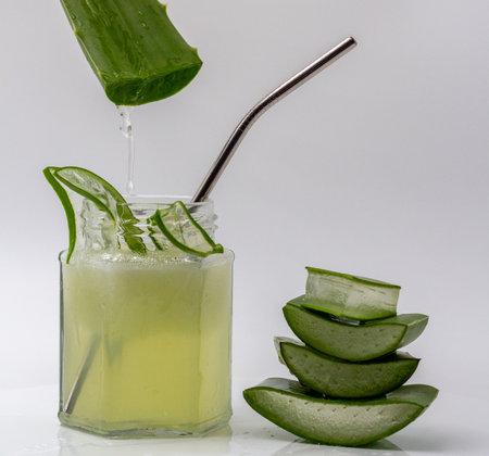 Aloe vera gel dripping on a jar of aloe vera juice with sliced and stacked aloe vera isolated on white background.の写真素材
