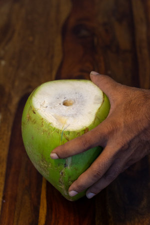 A close-up photo of a person's hand holding a tender coconut against a wooden platform.の写真素材