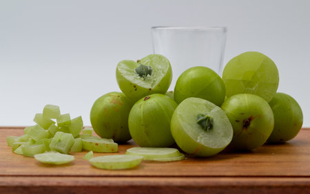 Front shot of a glass of Amla juice ,chopped amla and whole amla placed on a wooden chopping board.