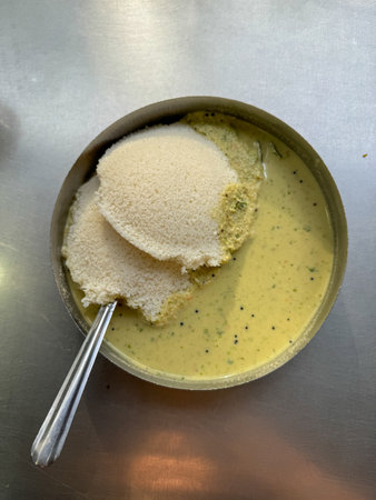A photo of a plate of Idli and chutney with a spoon on a table