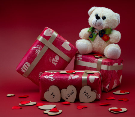 Wrapped gift boxes with a teddy on a red background with small heartsの写真素材