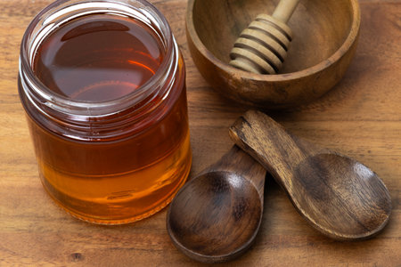 Wooden honey dipper kept in an empty bowl with wooden spoons and a honey jar on a wooden board.の写真素材