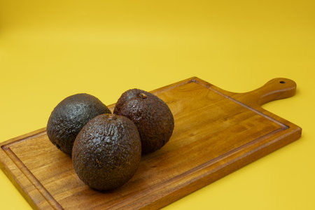 Close up of whole Avocados placed on a wooden board against a yellow background