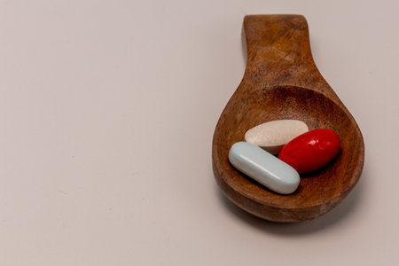 Soft red and yellow gelatin capsules with blue and white tablet in a wooden spoonの写真素材