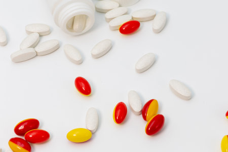 Close up of soft red and yellow gelatin capsules and white tablets scattered with the bottles on a...