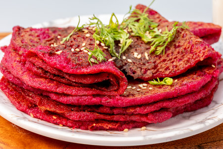 Beetroot pancakes stacked and garnished with sesame seeds, coriander and served with hung curd dip on a wooden trayの写真素材