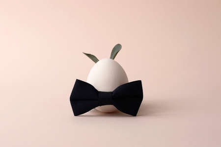 Easter egg with bow tie and ears from natural laves on the trendy pastel background.Minimal...