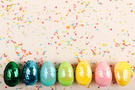 Colorful glossy easter eggs with sequins.Vivid pastry topping on the pastel background.Festive background.Festive flat lay.Creative row of multicolored eggs.の写真素材