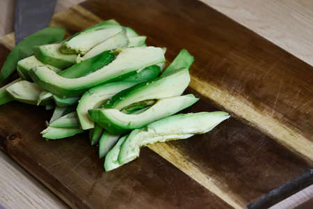 Sliced fresh avocado slices on a wooden board. Knife blade on the background.Copy space for...