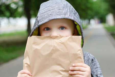 Funny blondheared toddler eating georgian bread with appetite on the street.Holding its in the paper craft package. Closeup photography of funny boy.Copy space for text.の写真素材