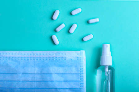 A pile of white pills,medical face mask and antiseptic on the trendy mint background.Medicine and covid concept.Copy space for text or design.Coronavirus or flu prevention.の写真素材