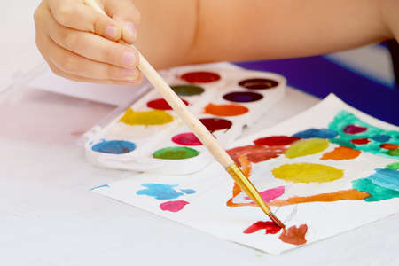 A child holds a paintbrush, along with paints and drawing tools.Close up photography of a child's hand.Back to school concept.Copy space.の写真素材
