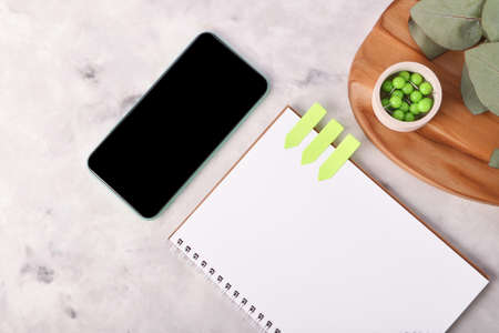 Blank notebook on the marble background.Mobile telephone with black screen.Fresh eucalyptus branch...