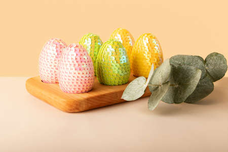 Multicolored glossy handmade eggs from sequins in the wooden tray.Eucalyptus branch behind.Trendy...