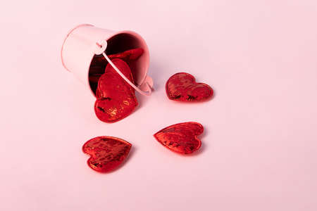 Little decorative pink bucket full of red hearts lies on the pretty pink background.Hearts around...