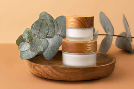 Skin care packaging with cream staying on each other in the wooden plate.Eucalyptus branch behind.Pastel isometric background,organic concept.の写真素材