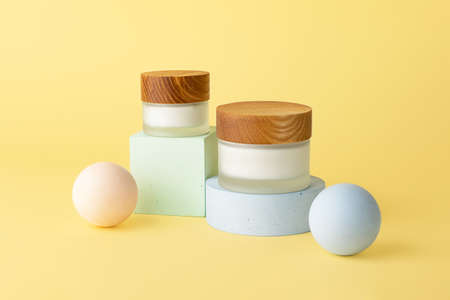 Two skin care packaging boxes with white cream,staying on the geometrical podiums.Pastel background,mockup for advert with copy space.Wooden covers,zero waste package.の写真素材
