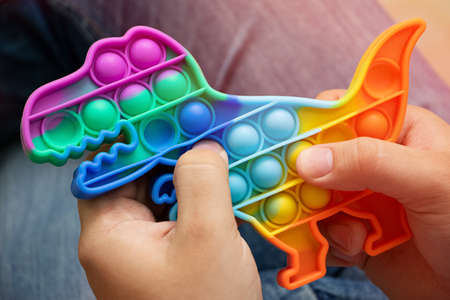 Anonymus adult hold in his hands new silcone toy pop it in shape of dinosaur.New sensory antistress toy for children and adults.Trendy rainbow coloring.の写真素材