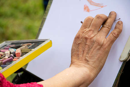 Street artist holding a box with multicolored crayons and pencils for drawing.Close up photography of hands and drawing supplies.He drawing behind the easel with white paper.の写真素材