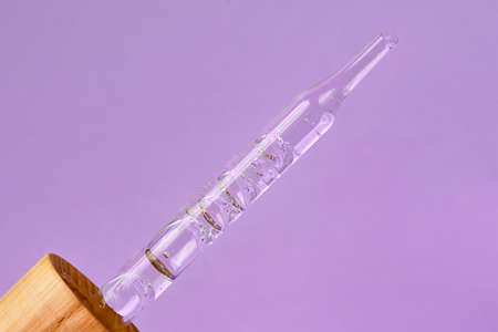 Closeup photography of the pipette with dripping gel.Zero waste wooden cover, purple background.Cosmetics mockup concept.の写真素材