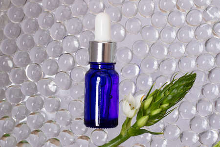 Cosmetics bottle from blue glass, top view.Transparent hydrogel balls around them.Green branches with white flower, like frame.Organic concept.の写真素材